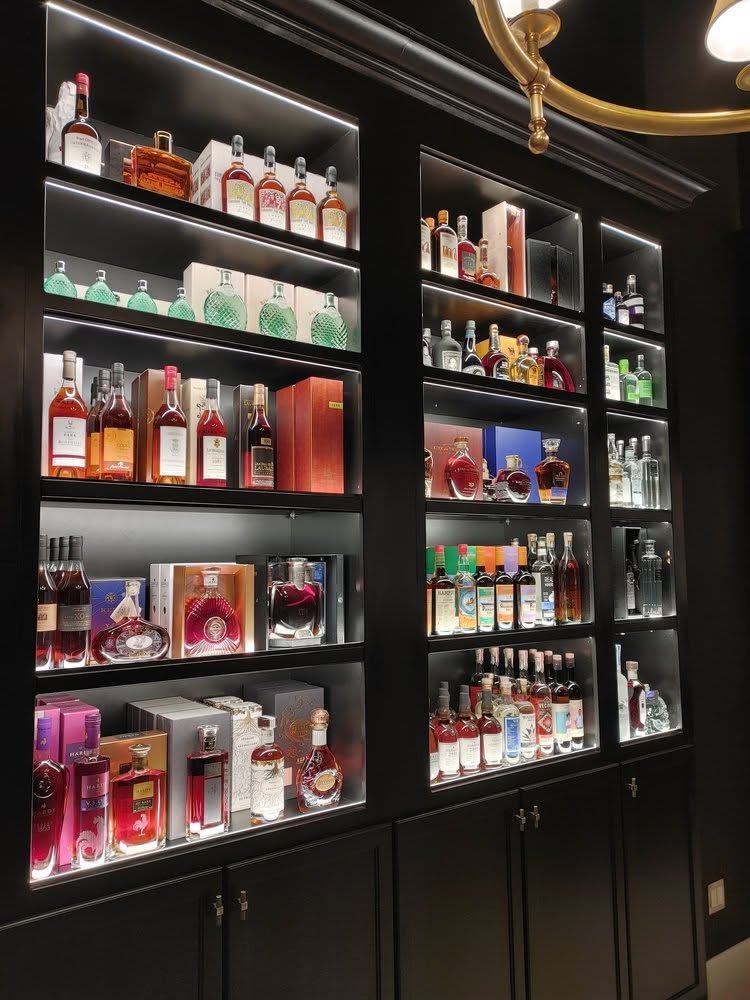 Black bar shelves lined with assorted liquor bottles and glassware, illuminated by warm lights.