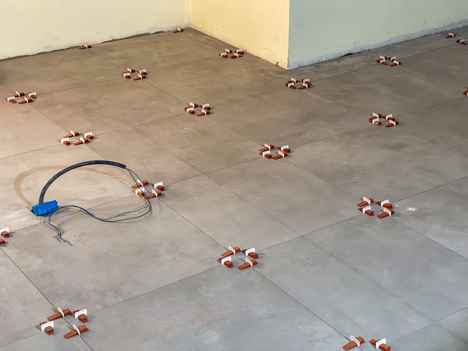 Floor tiled with several small flower-shaped markers and a blue cable near a corner wall.
