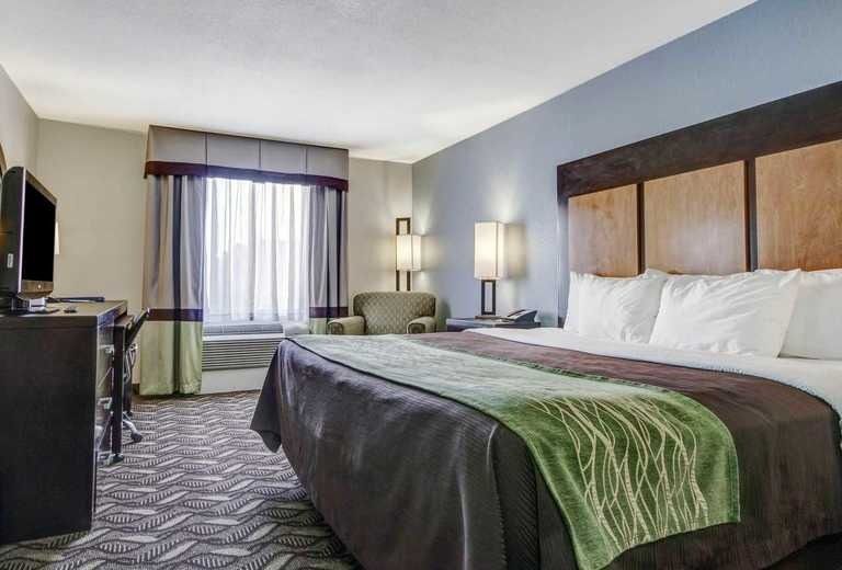 A hotel room with a king size bed , television , desk and chair.