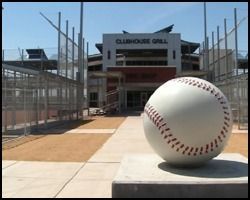 A large baseball is sitting on a concrete pedestal in front of a clubhouse grill.