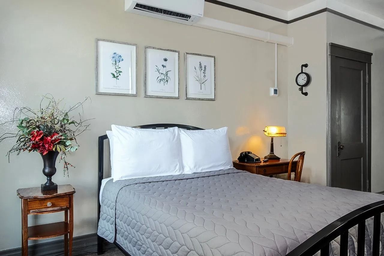 A bedroom with a bed , nightstand , lamp and a vase of flowers.