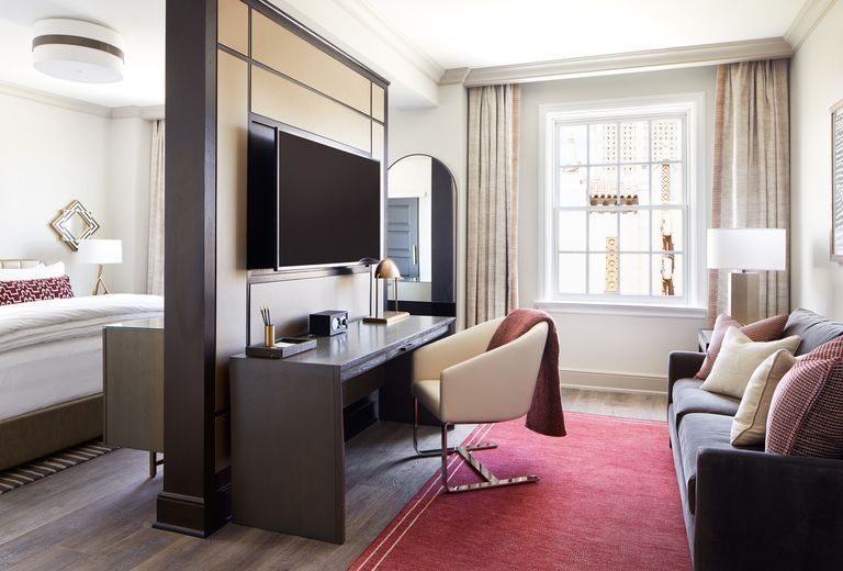 A hotel room with a couch , chair , desk and television.
