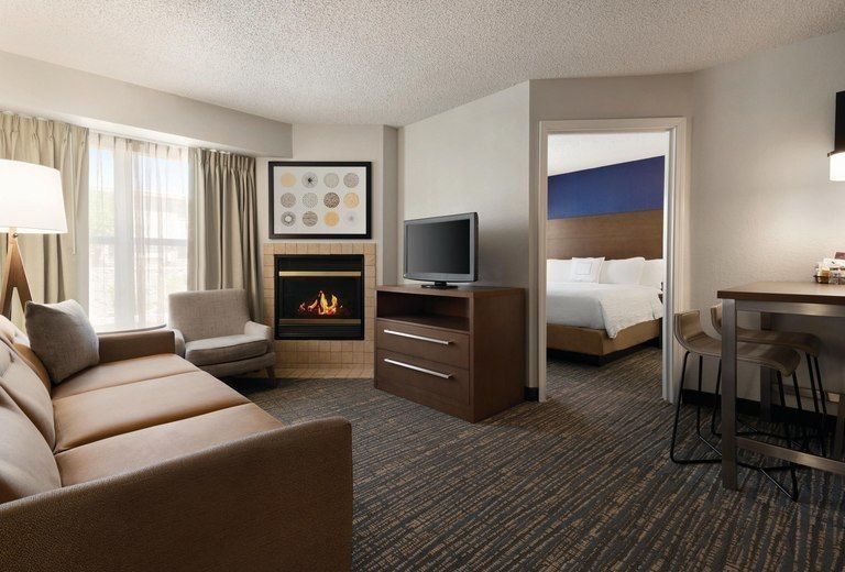 A hotel room with a couch , chair , television and fireplace.