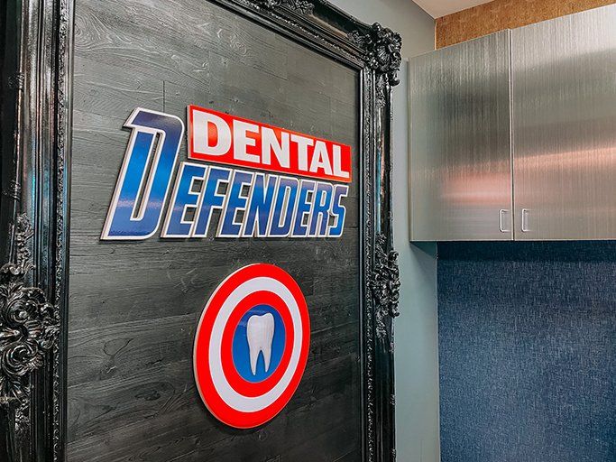 Dental Defenders sign beside a red-and-blue tooth logo on a black door in a clinic hallway