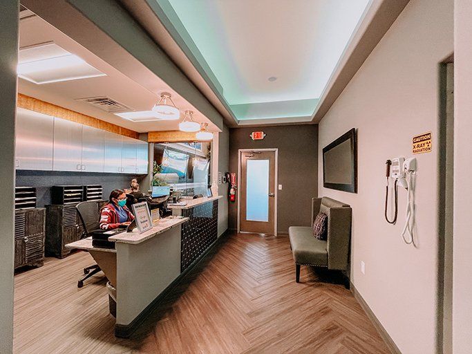 Modern clinic reception with front desk, waiting chair, and wall-mounted phone along a bright hallway
