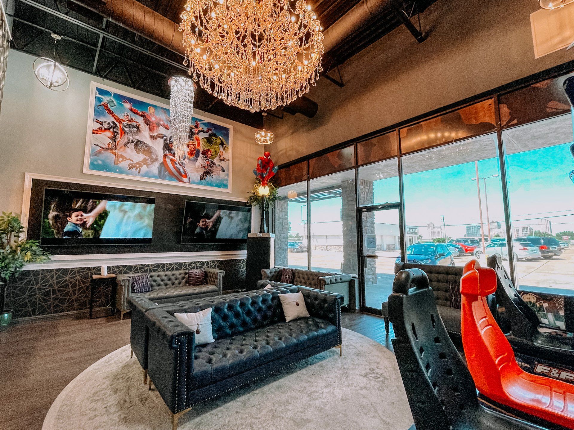 Modern lounge with black sofas, chandelier, red chair, wall art, and large windows overlooking a street