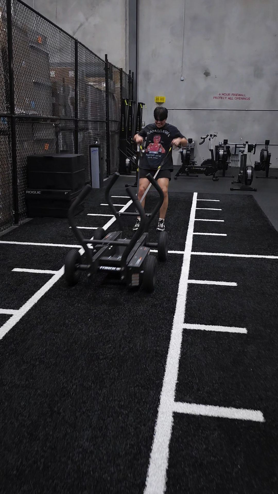 A person lifting a barbell overhead, wearing wrist wraps, green weight plate visible.