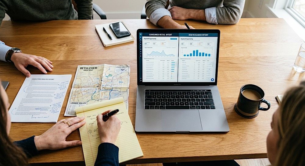 People around a wooden table reviewing papers and a laptop with charts and graphs.