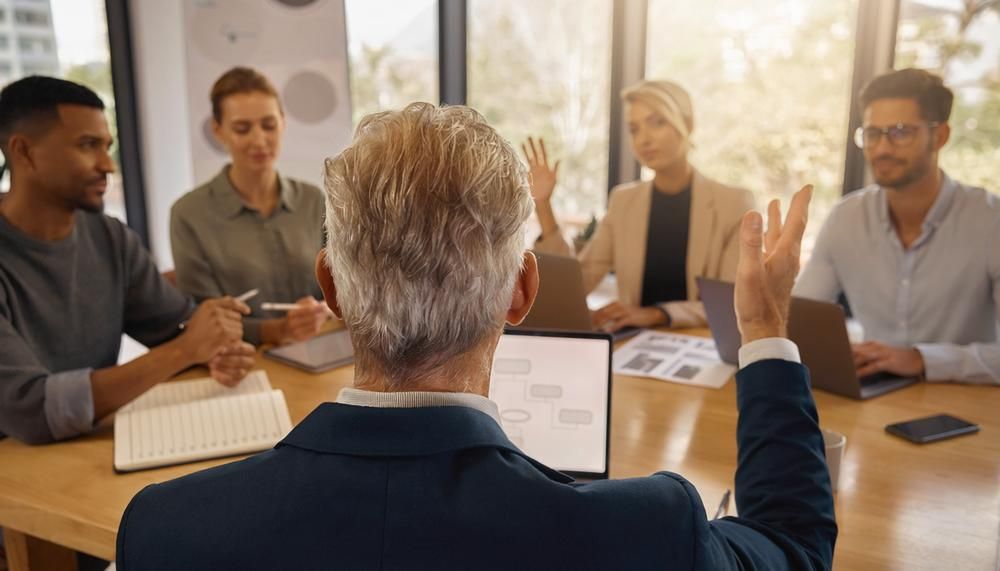 Business meeting around a conference table, with one speaker addressing colleagues in a bright office.