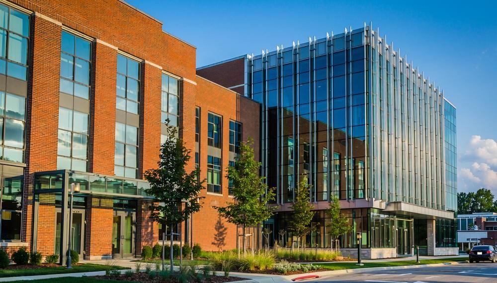 Modern brick-and-glass building exterior with trees and a clear blue sky