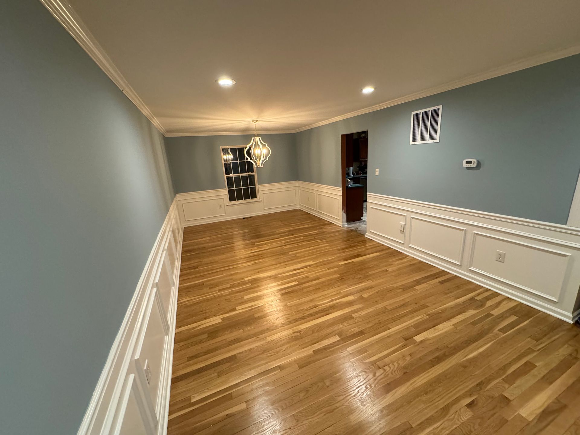 Empty living room with hardwood floors, blue walls, white wainscoting, and recessed ceiling lights.