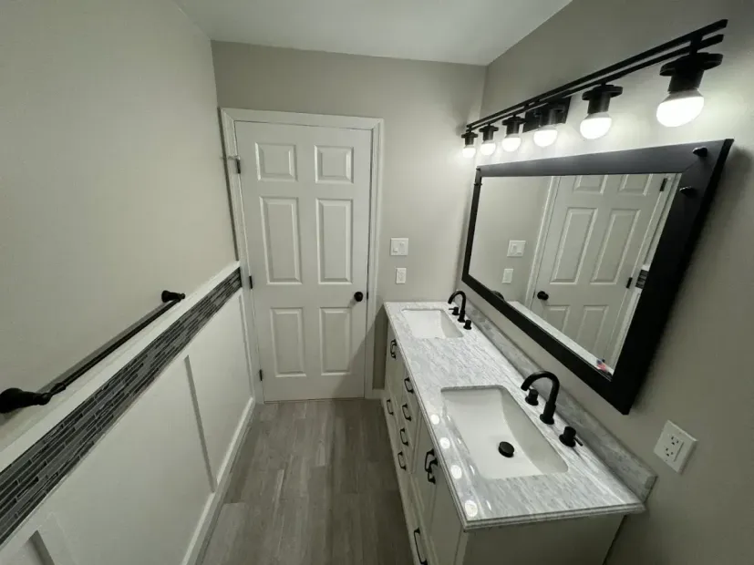 Accessible bathroom with sink, mirror, lights, and grab bars along a narrow hallway.