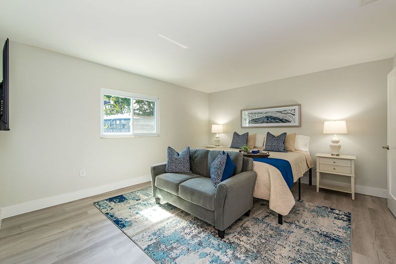 Bright bedroom with gray sofa, blue rug, bed, nightstands, and wall art in soft neutral tones