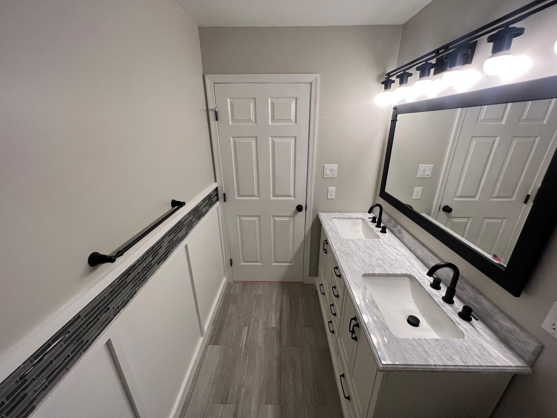 Narrow bathroom with vanity, large mirror, white walls, gray floor, and towel bar along the left side.