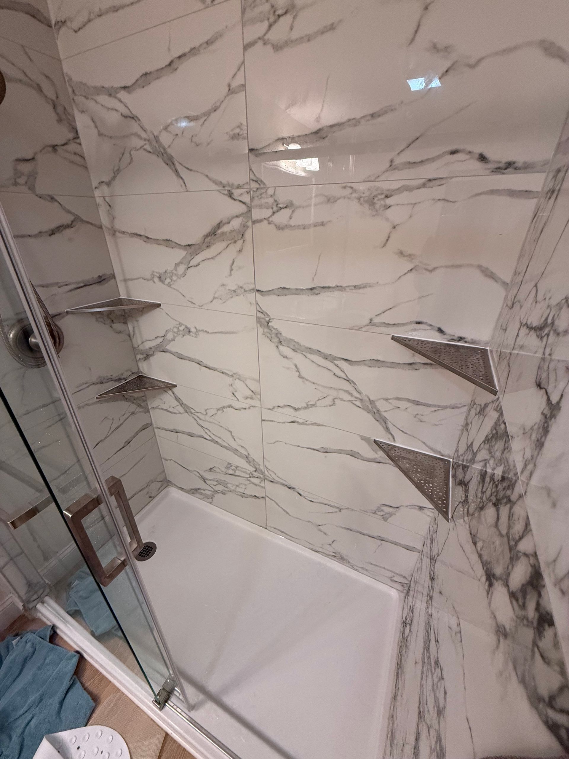Modern bathroom with white bathtub, glass shower door, and marble-patterned wall tiles.