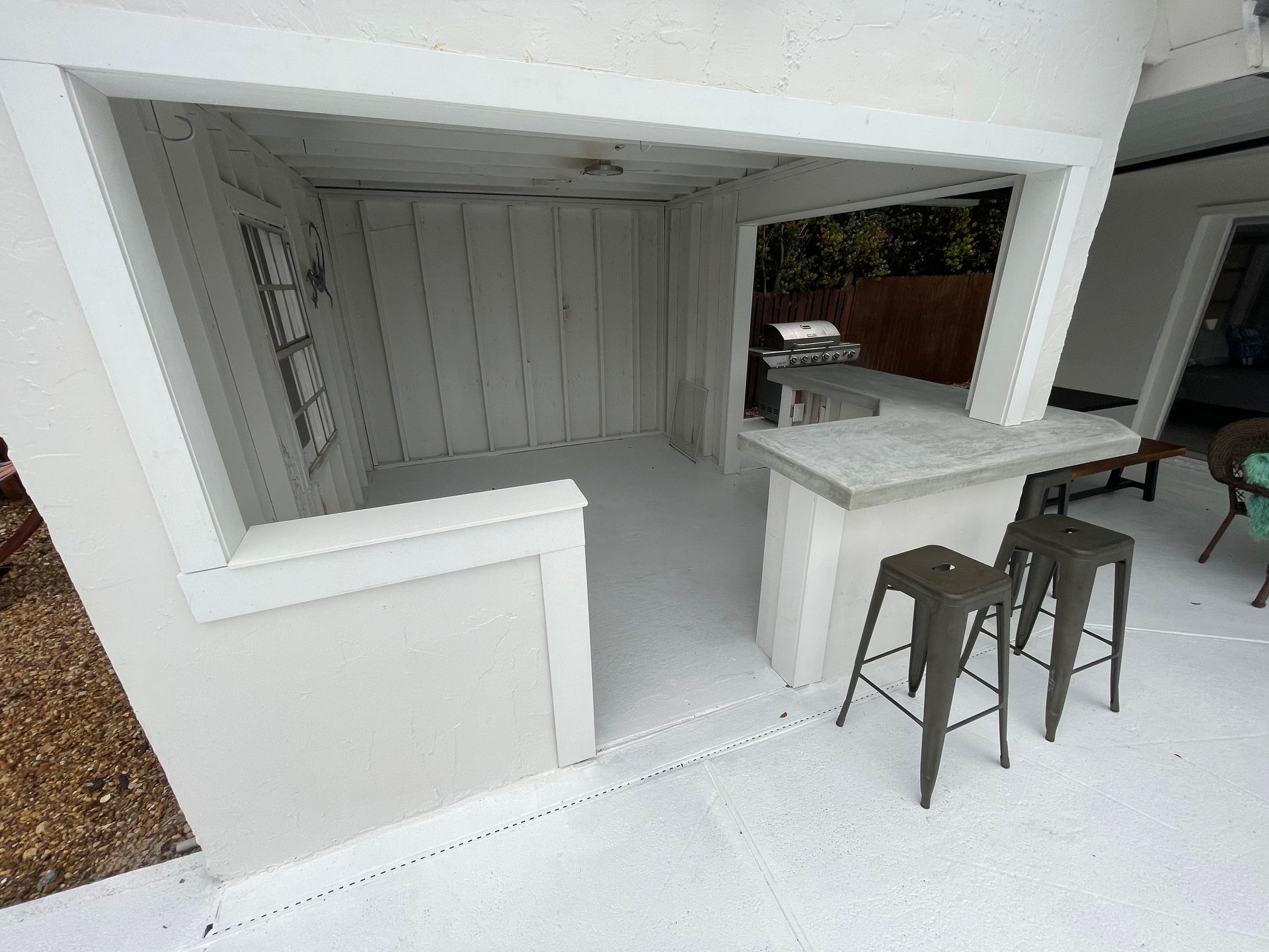 White outdoor bar alcove with counter, two stools, and open side seating area