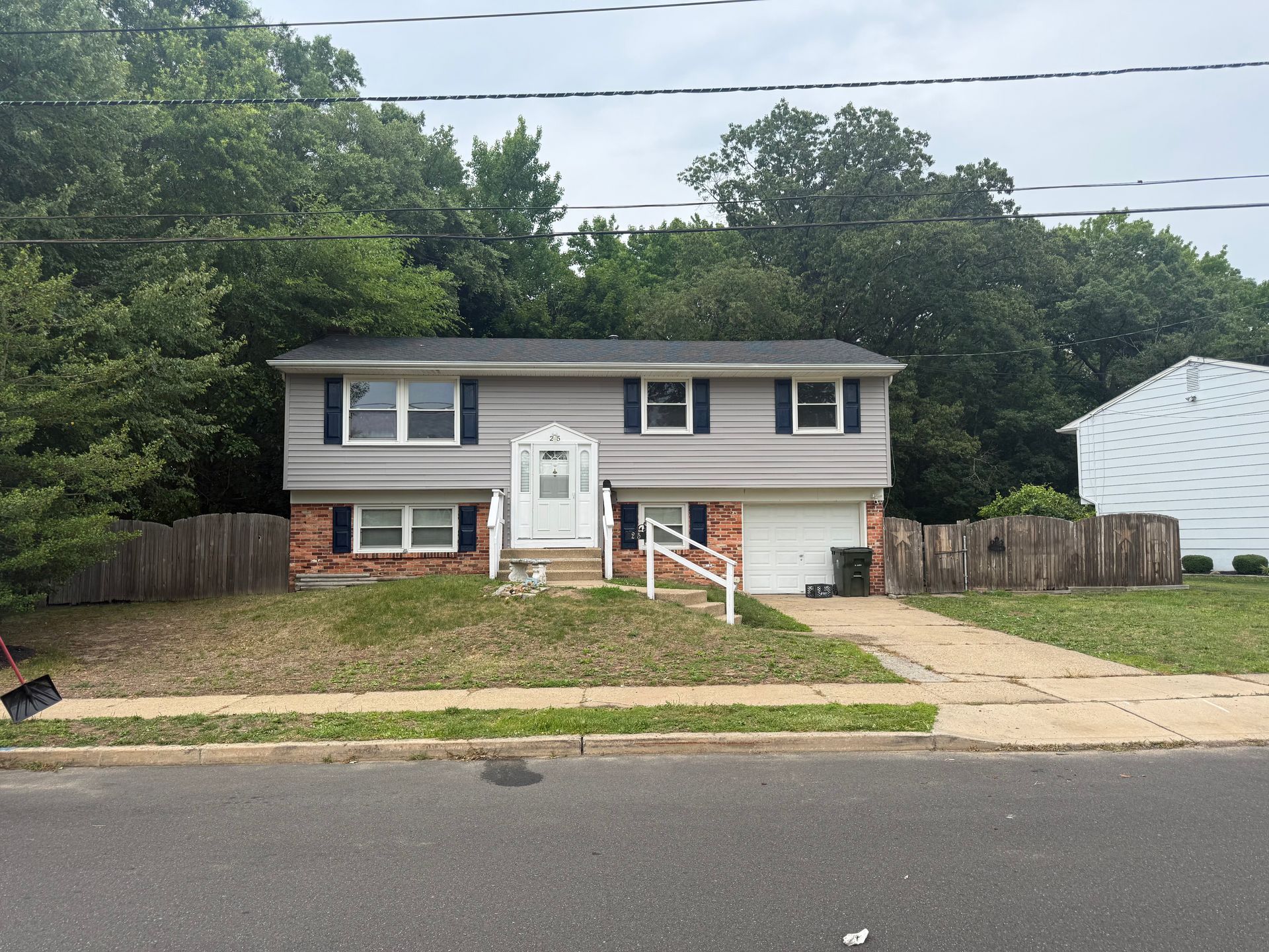 Suburban split-level house with gray siding, brick lower facade, and a front driveway under overcast skies