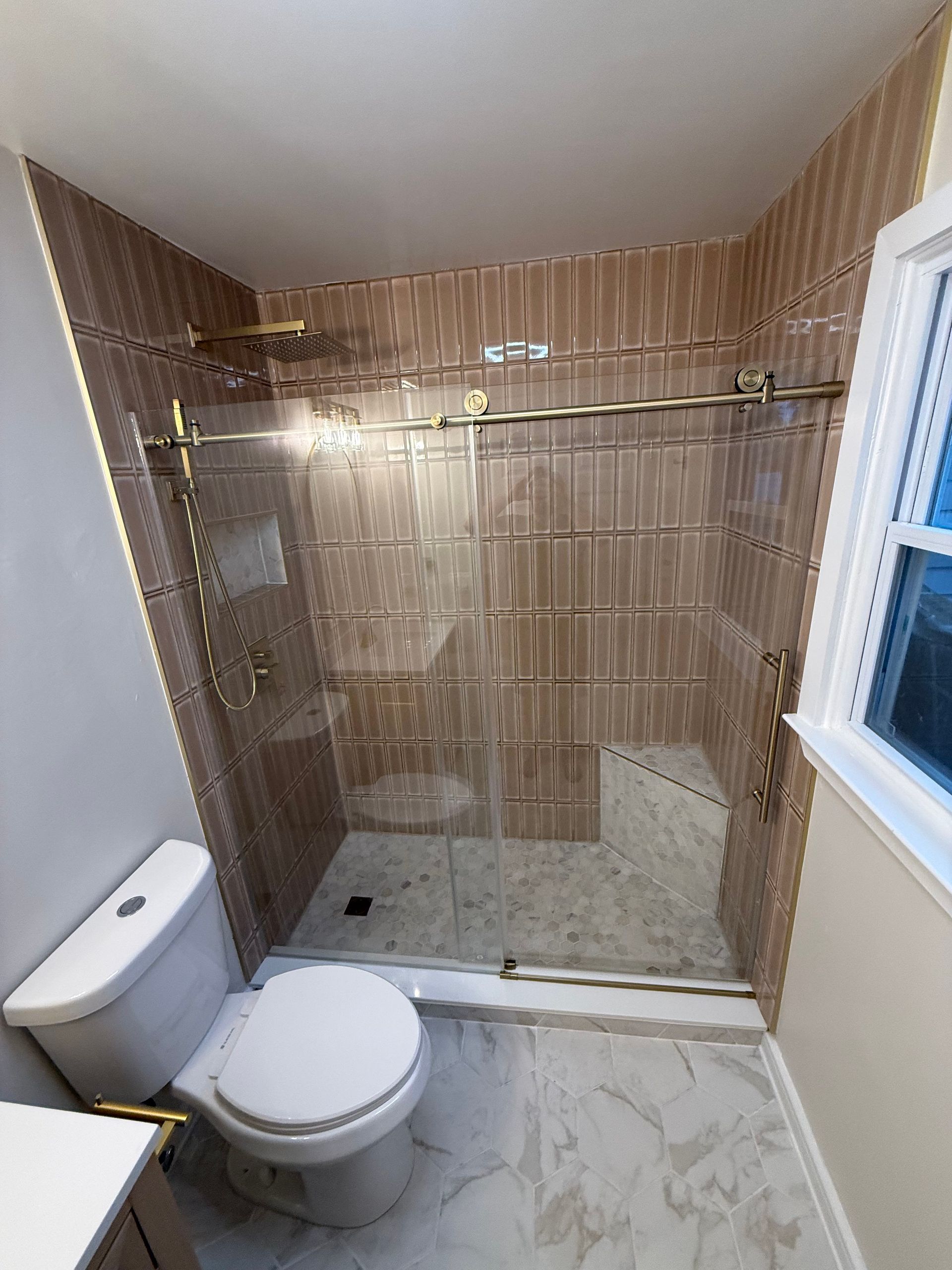 Small bathroom with a glass-enclosed shower, toilet, tan tile walls, and marble-pattern floor.