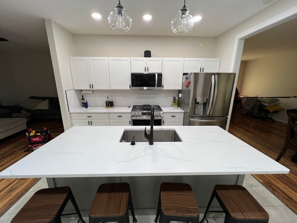 Modern white kitchen with large island, stainless steel appliances, and pendant lights