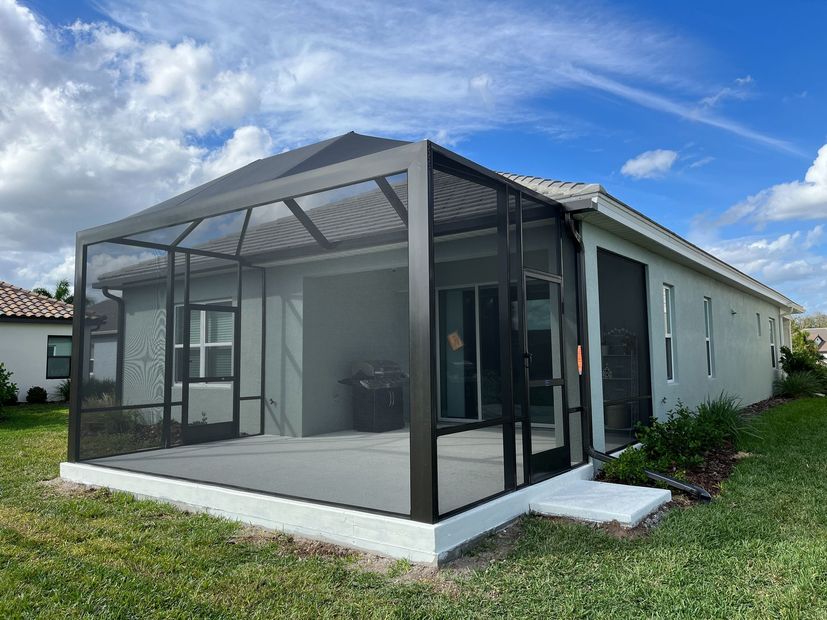Screened back patio on a white house with a gray roof and grassy yard under a blue sky