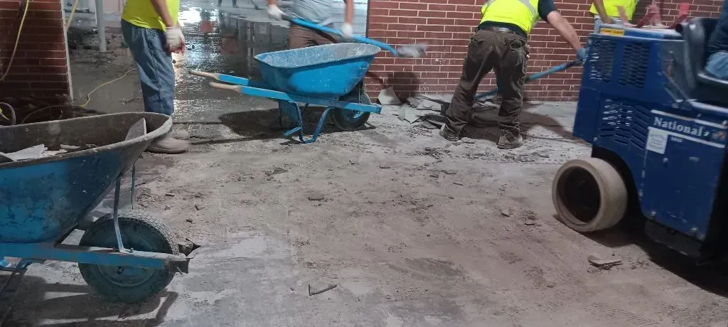 A person in blue jeans and red gloves uses a shovel to clear rocks and debris on a construction site.