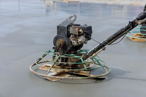 A walk-behind power trowel smoothing wet concrete on a construction site.