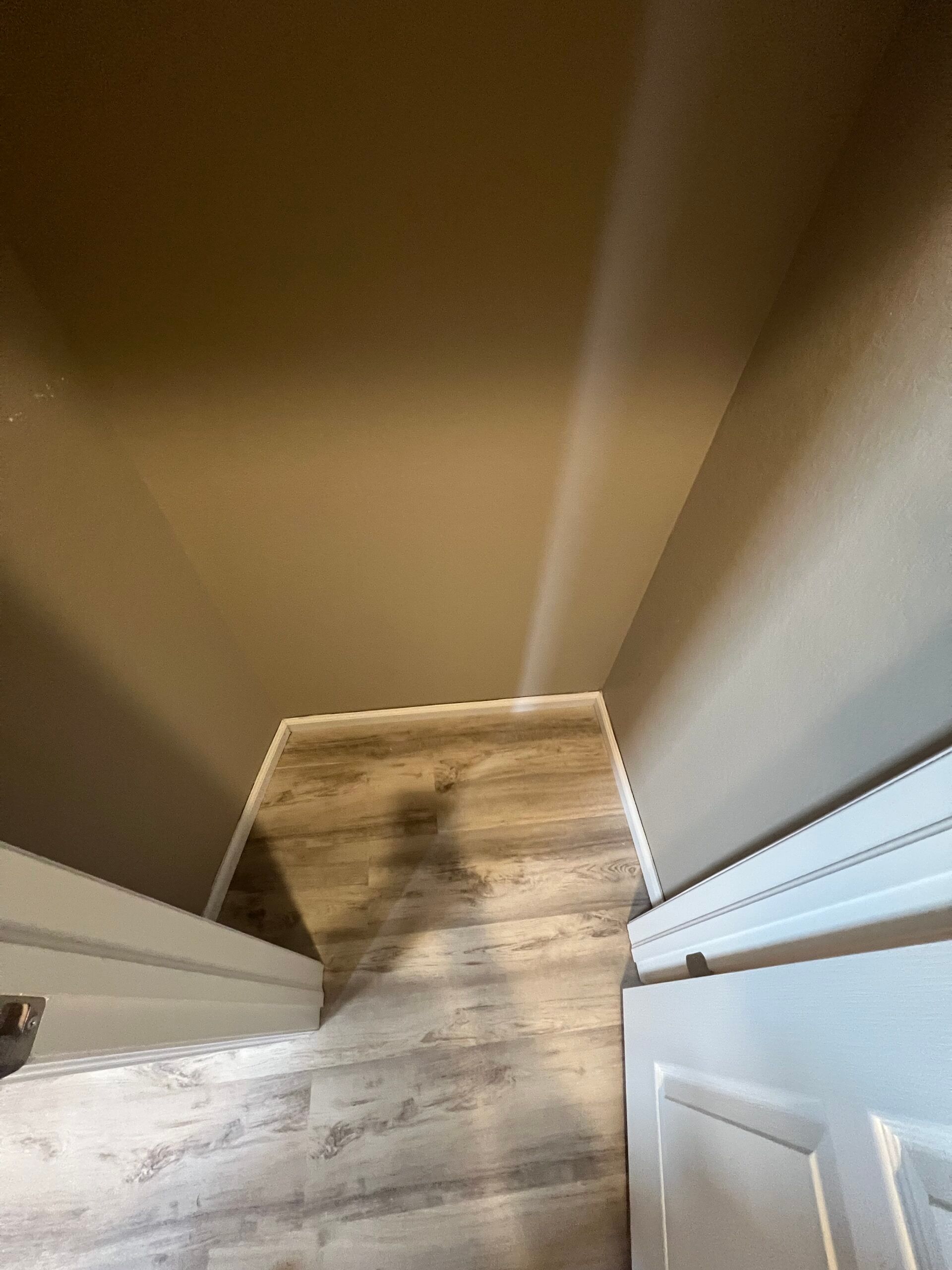 Top-down view of a hallway with wood flooring and a white door against tan walls.