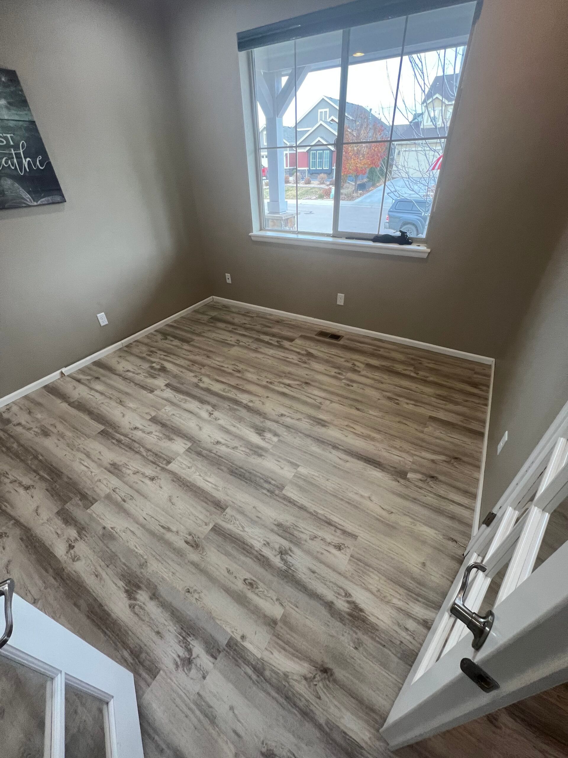 Empty beige bedroom with gray wood-look flooring and a window view of houses outside.