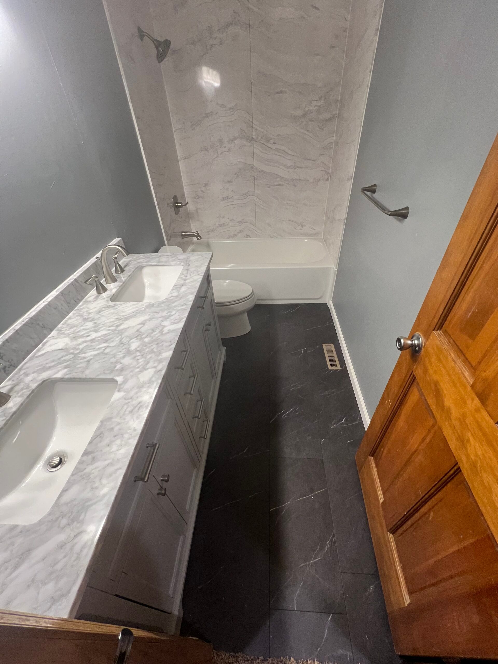 Narrow bathroom with granite vanity, wall mirror, dark floor, and wooden door partly open.