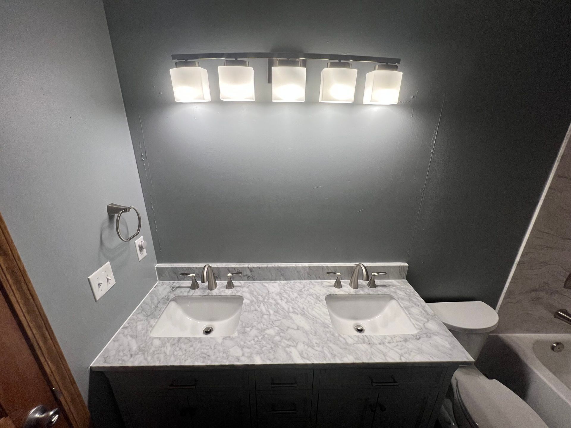 Modern bathroom with double sink vanity, marble countertop, and lit wall mirror.