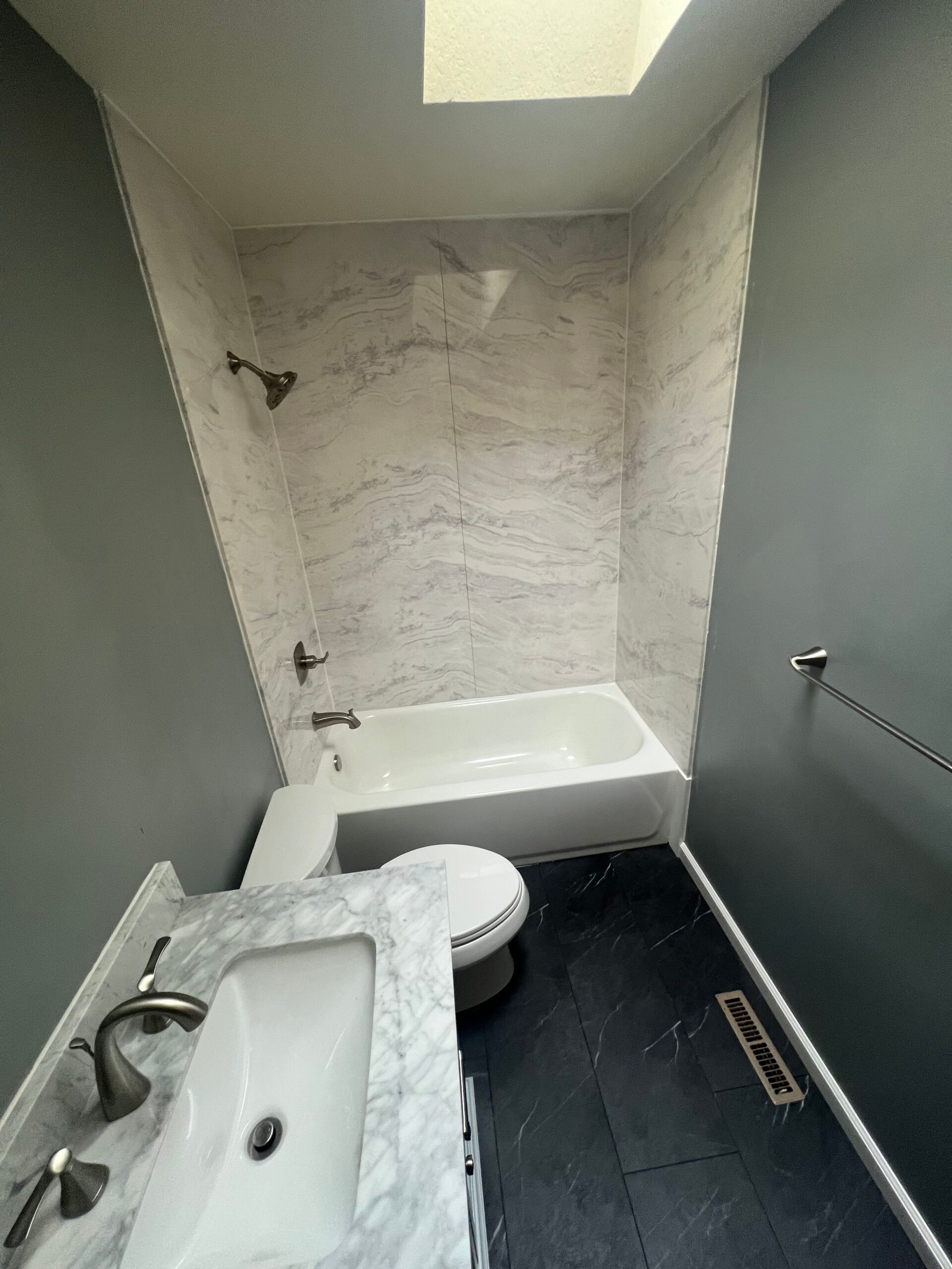 Small bathroom with shower-tub, sink, and toilet, white tile wall, black floor, and green walls