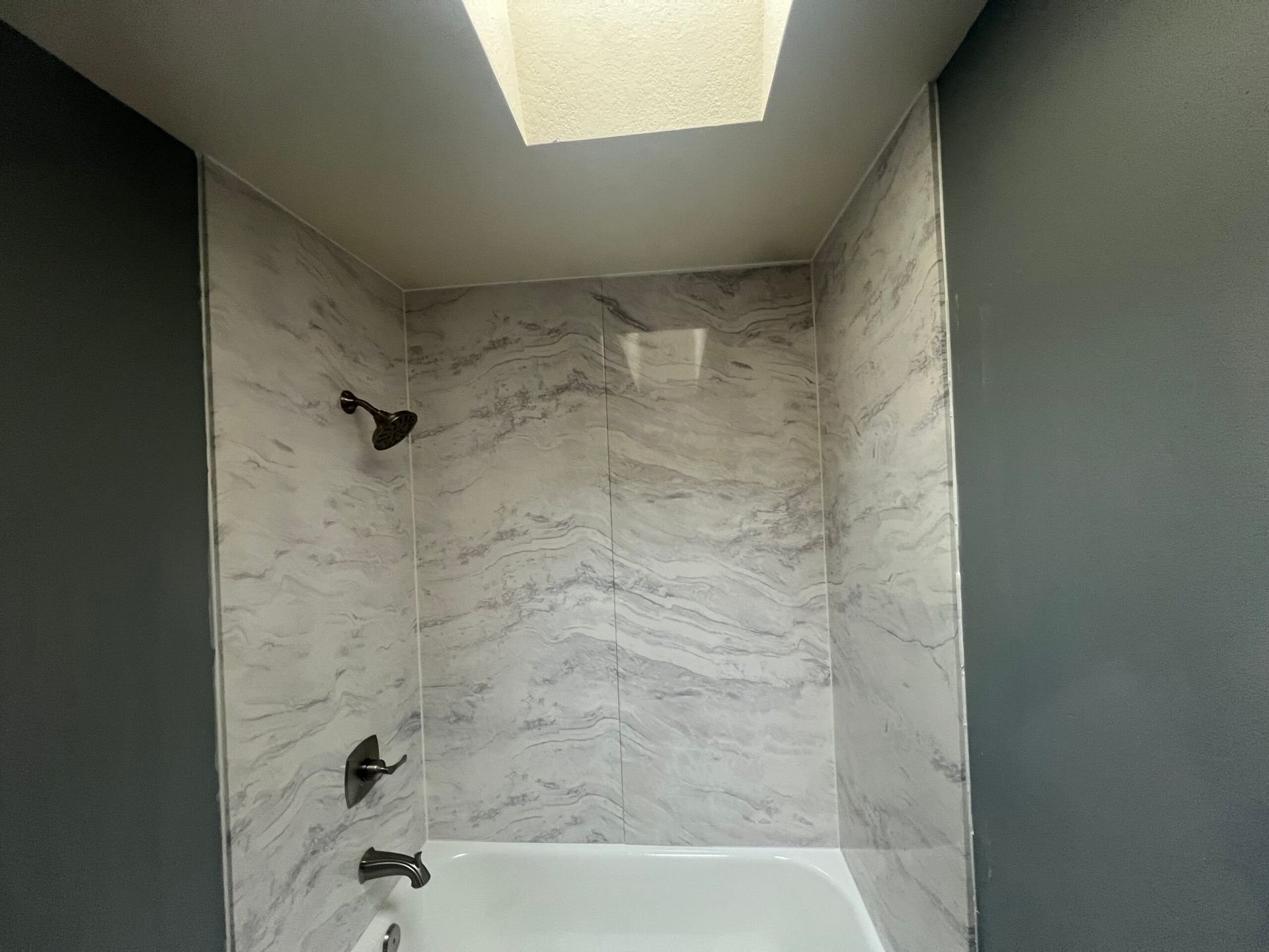 Modern shower stall with marble-pattern tile walls, two black fixtures, and a skylight above.