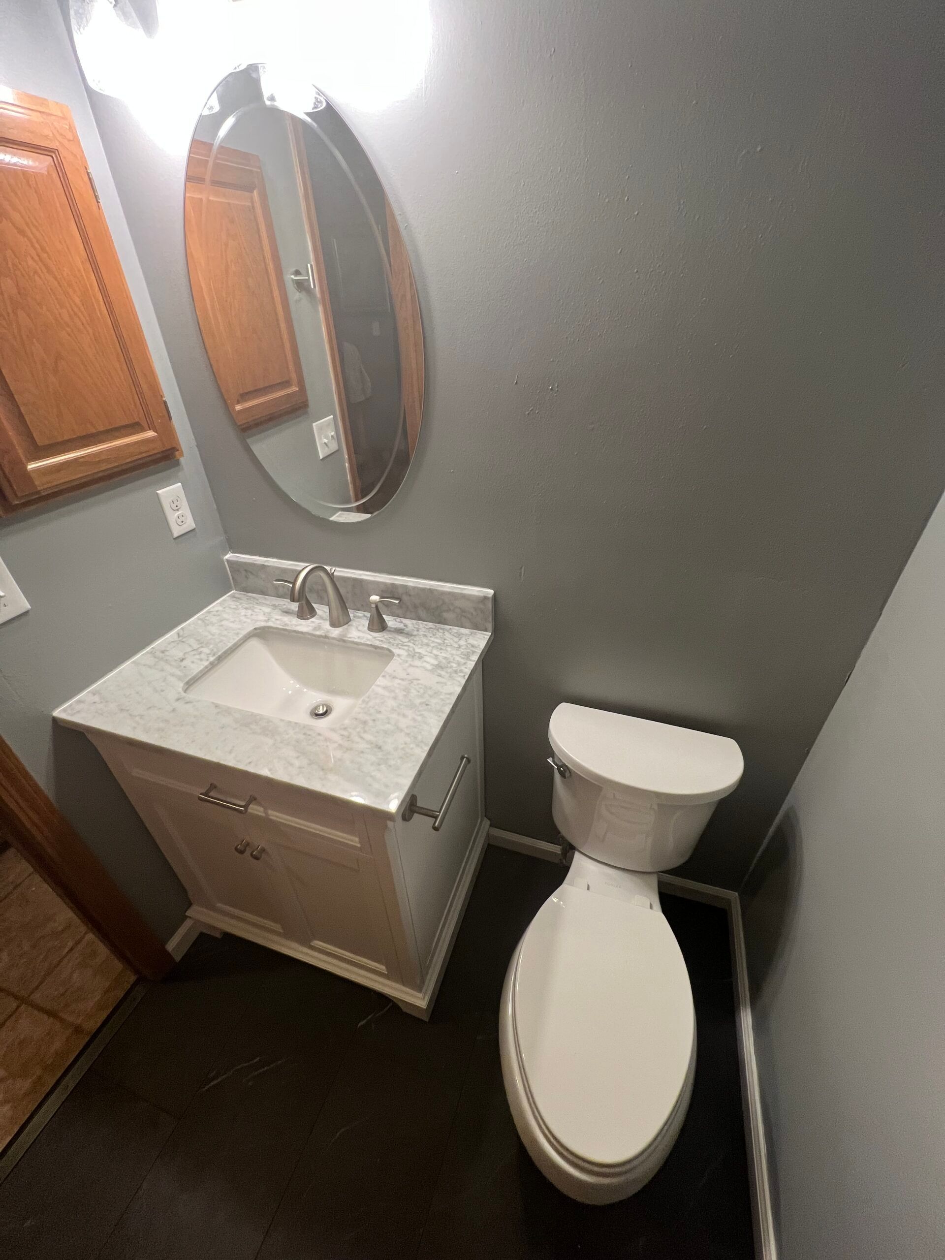 Small bathroom with white tub, sink, toilet, dark floor, and unfinished back wall.