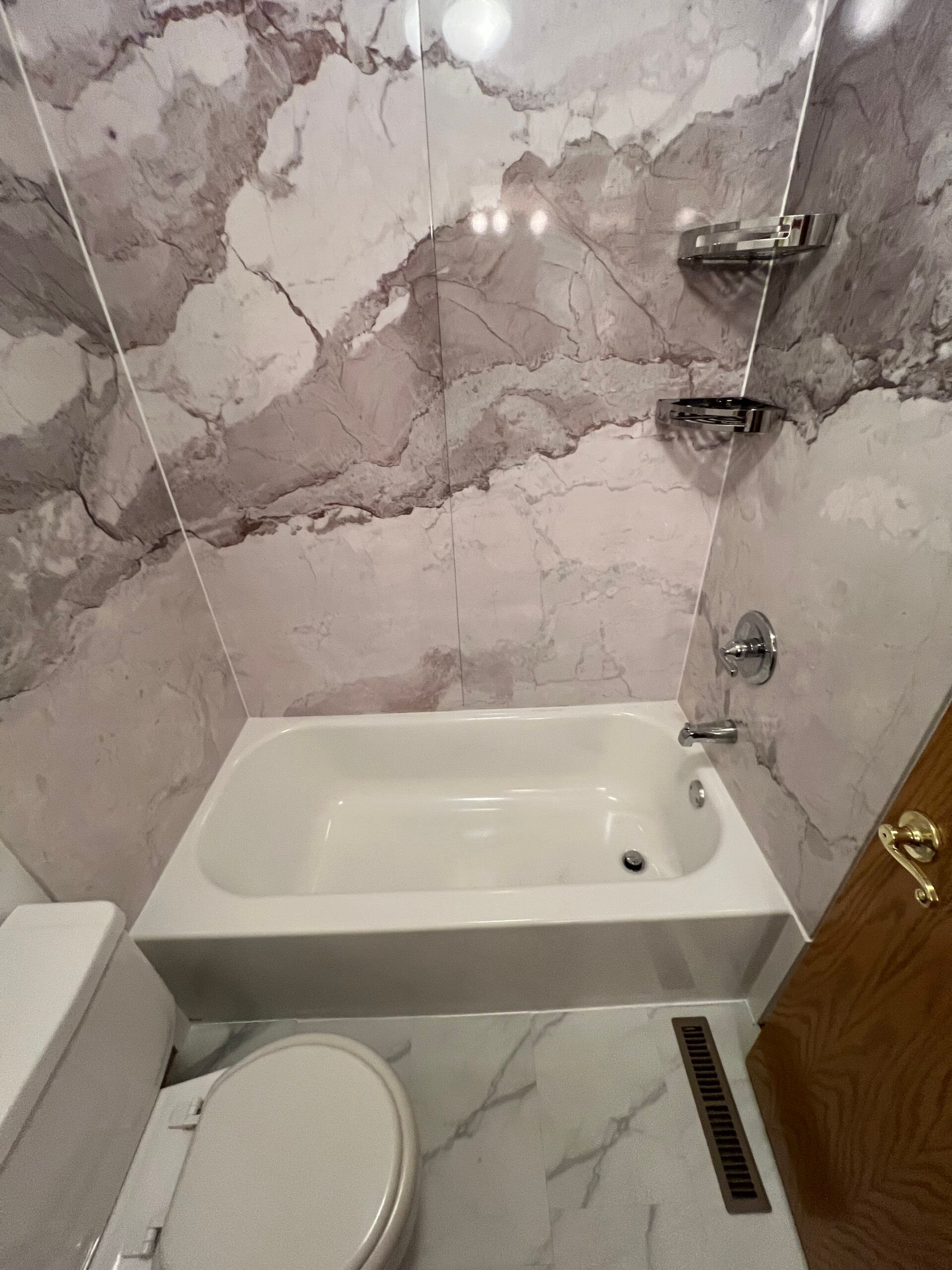 Small bathroom with a bathtub, toilet, marble-patterned wall, and shower fixtures.