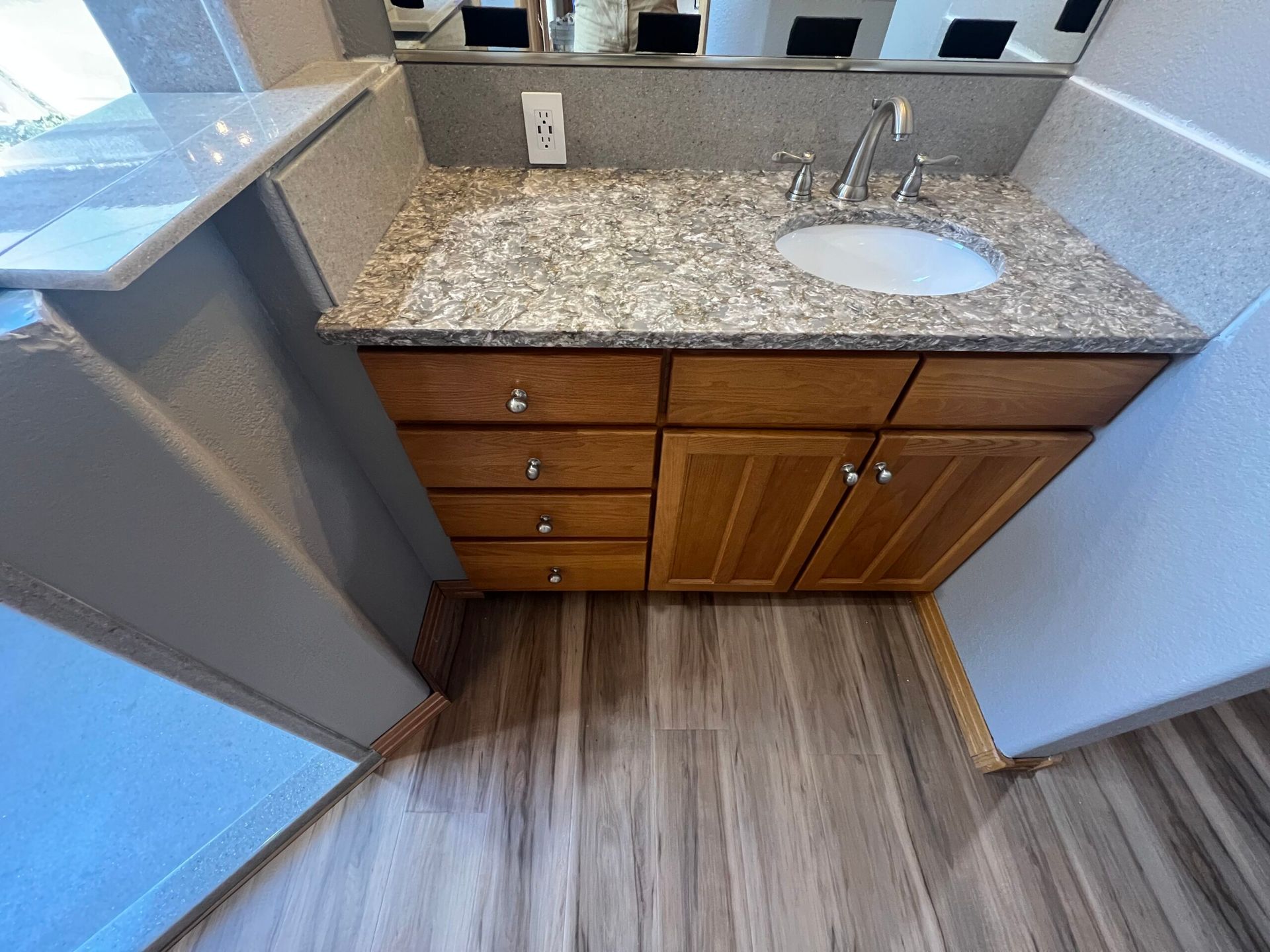 Small bathroom vanity with granite countertop, sink, mirror, and wooden cabinets under bright lighting