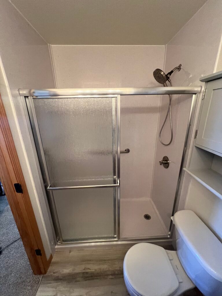 Small bathroom with a glass shower, toilet, vanity, and light wood floor