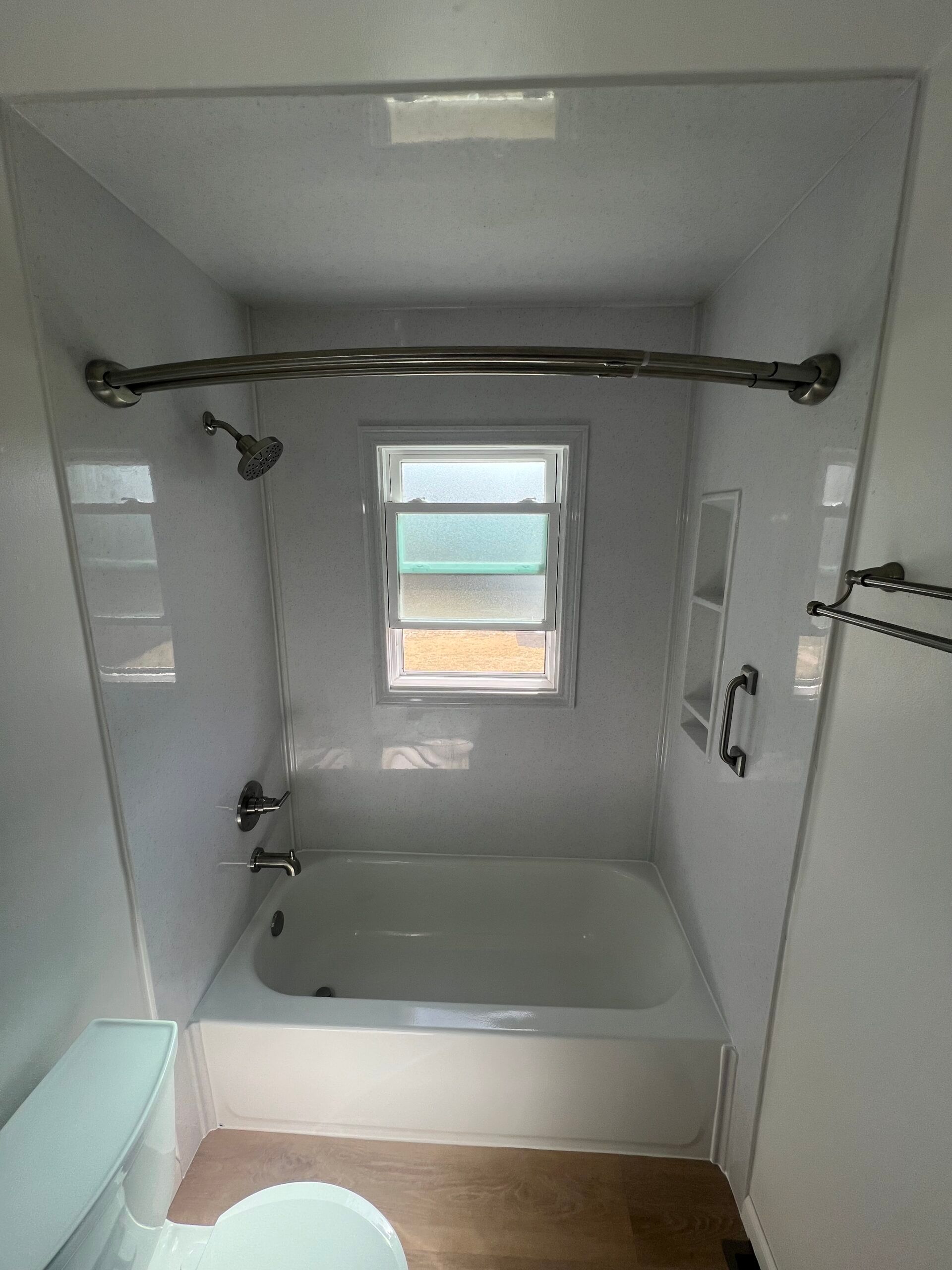 Small white bathroom with a bathtub, shower curtain rod, window, and grab bars.
