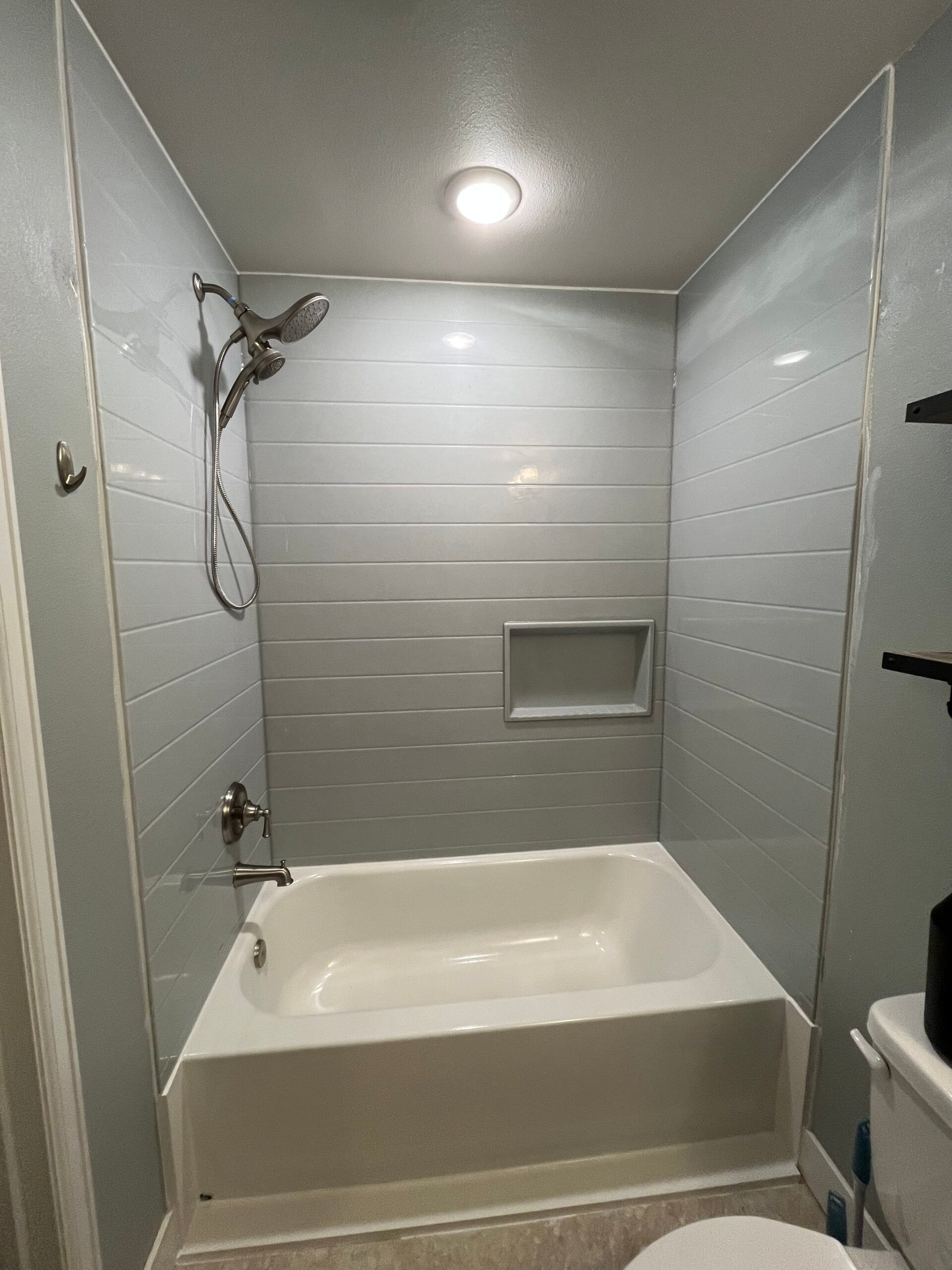 Small white-tiled bathroom with a bathtub, showerhead, and recessed wall shelf.
