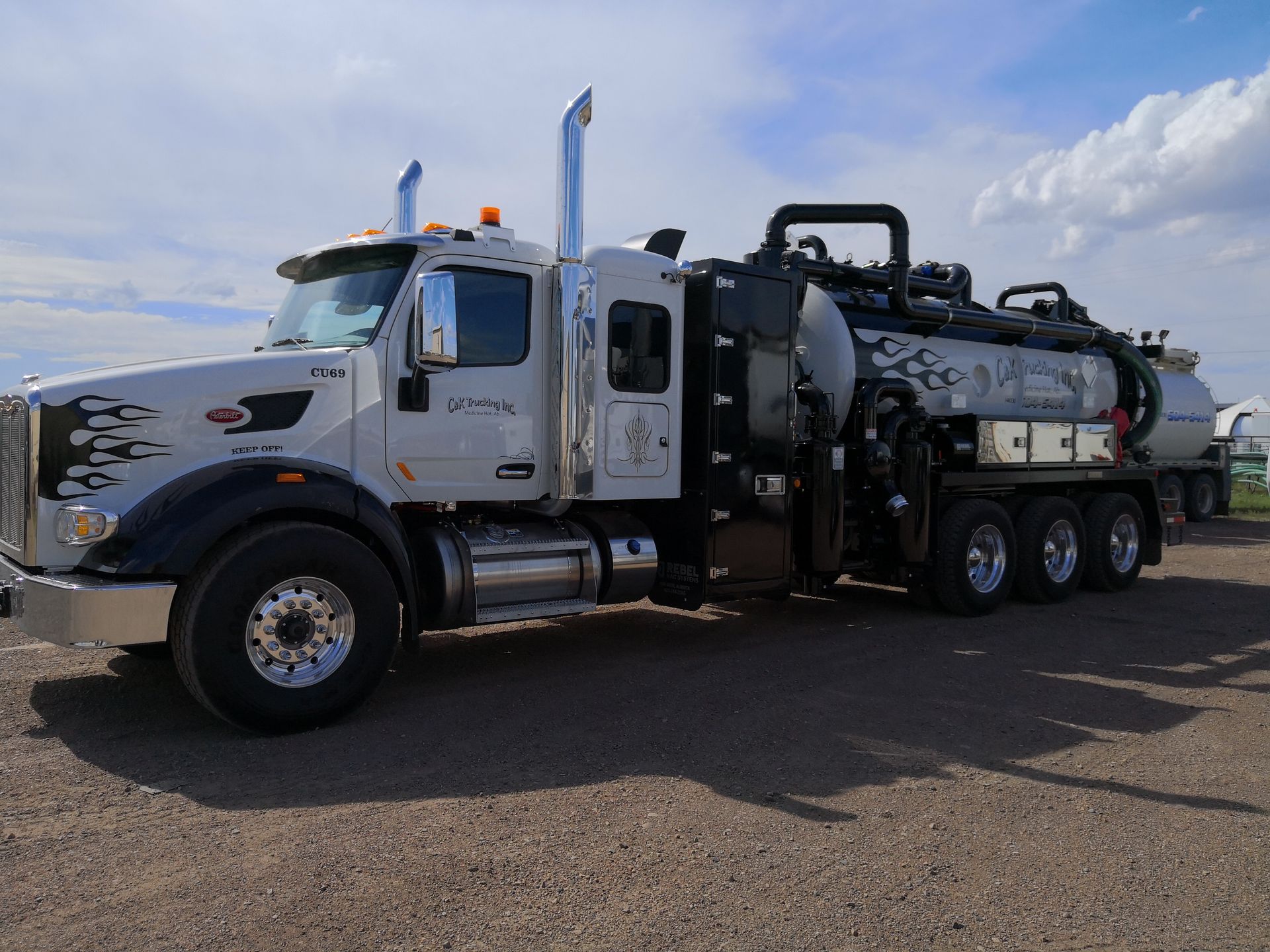 White vacuum truck with tanks parked on a gravel lot under a partly cloudy sky
