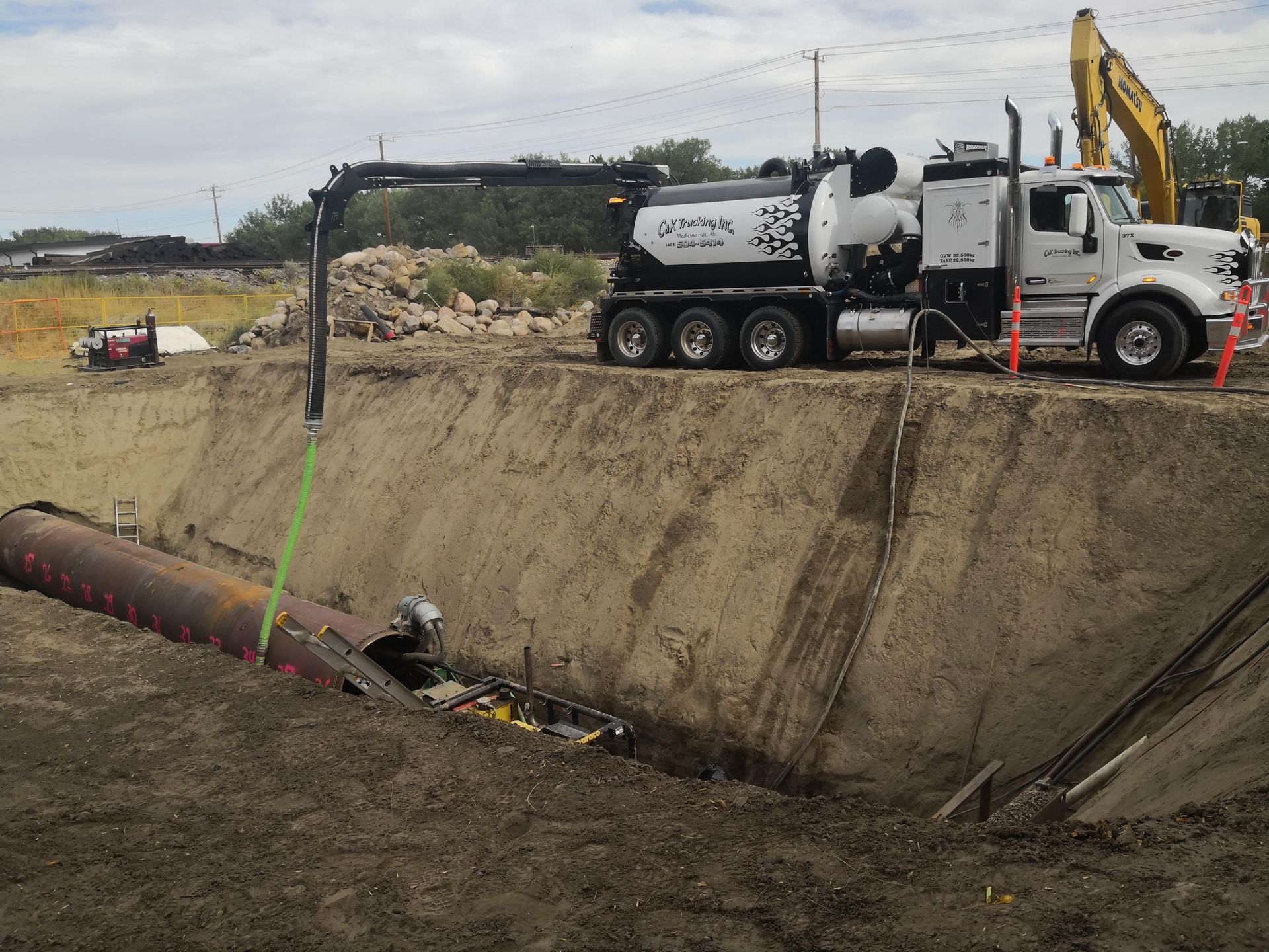 Construction truck and excavator at a trench beside a muddy slope in a work site.