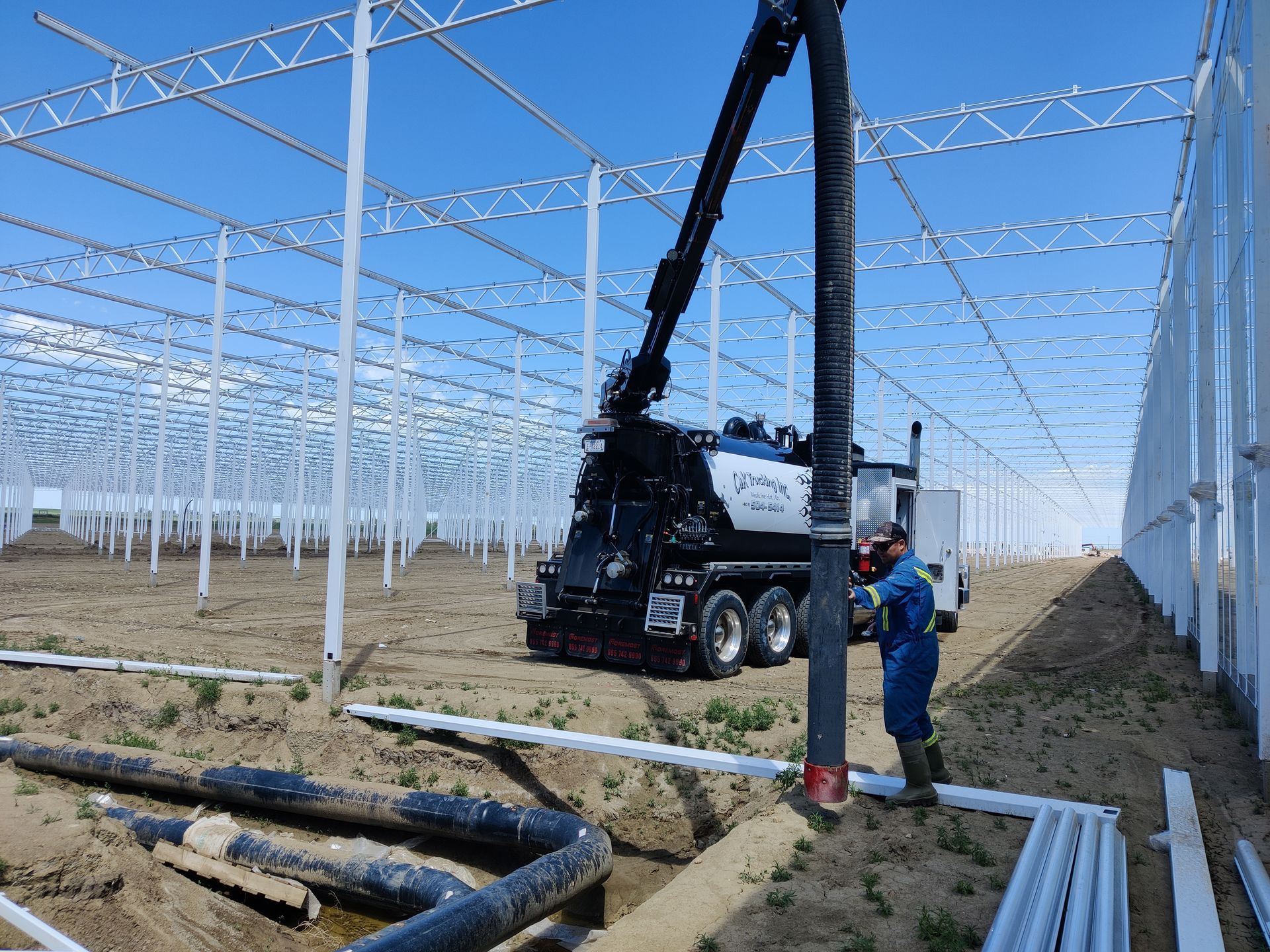 Worker operating crane beside large white greenhouse frame under construction