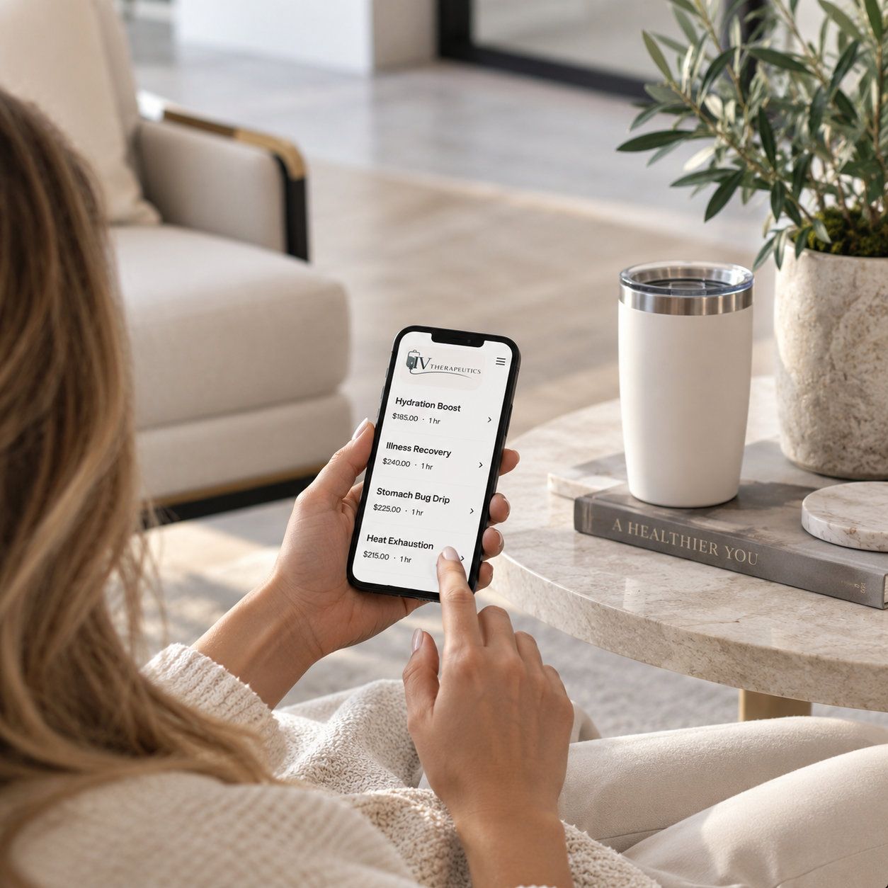 Person using a smartphone on a couch beside a coffee table with a tumbler and plant