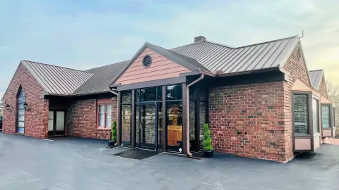 Brick commercial building with black-framed glass entrance and metal roof under a bright sky