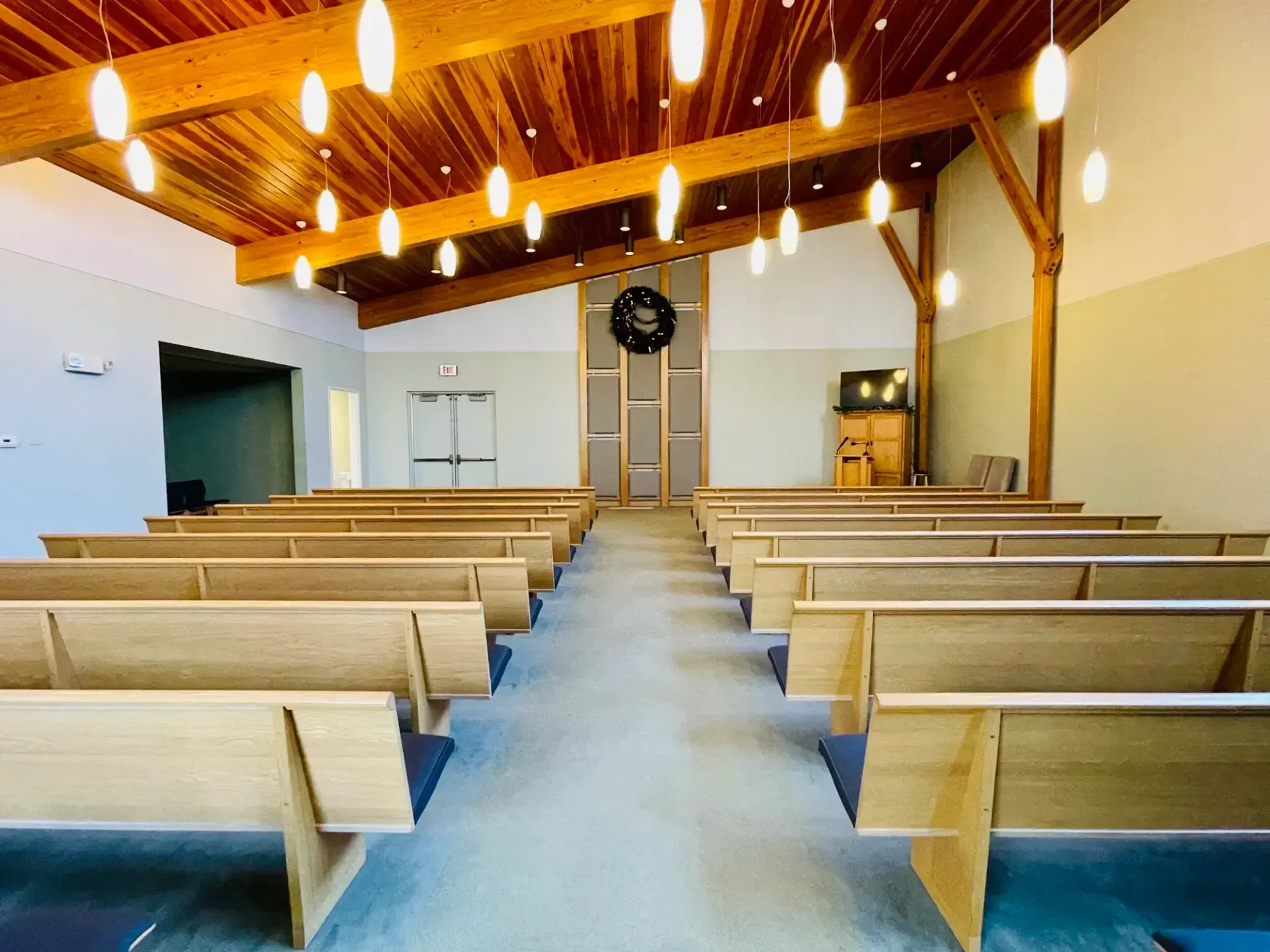 Empty church interior with wooden pews, sloped timber ceiling, and hanging pendant lights