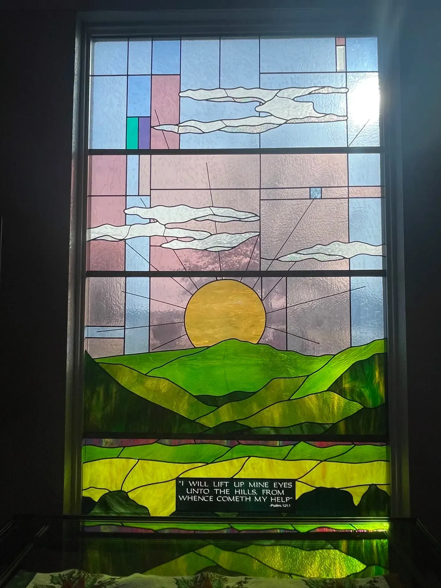 Stained-glass landscape with sun over green hills, clouds, and a pink-and-blue sky.