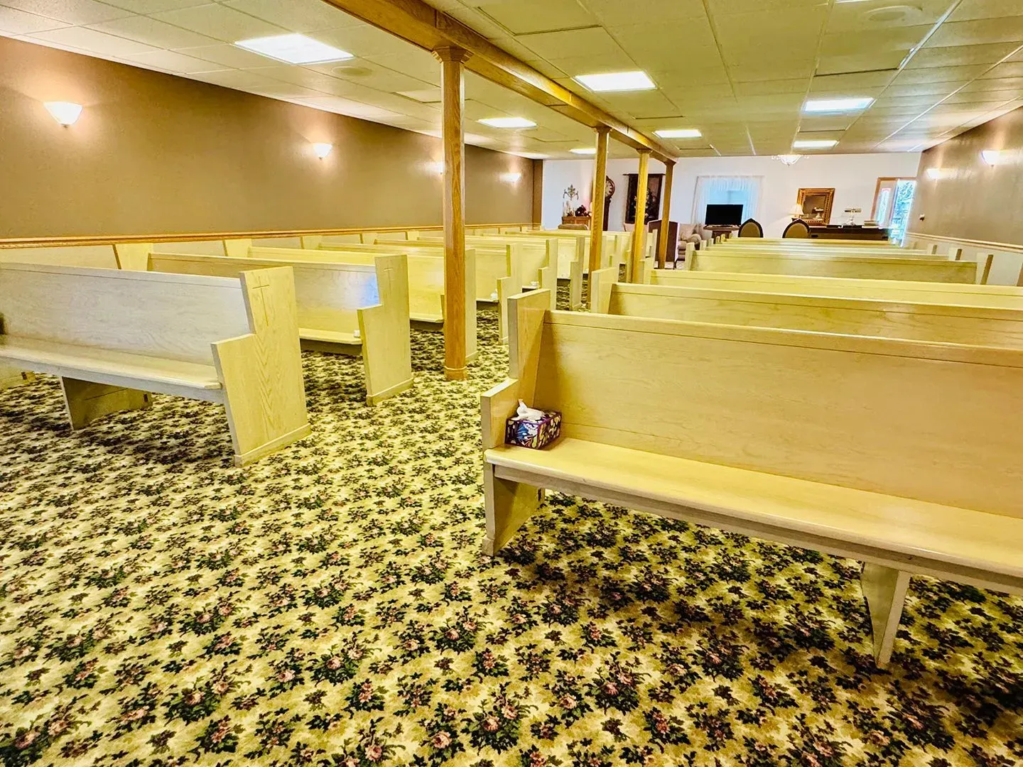 Empty church pews in a carpeted sanctuary with wooden columns and warm lighting.