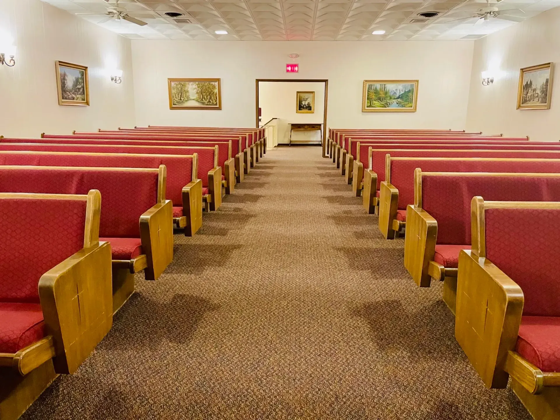Empty chapel with red pews, patterned carpet, and a central aisle leading to the altar