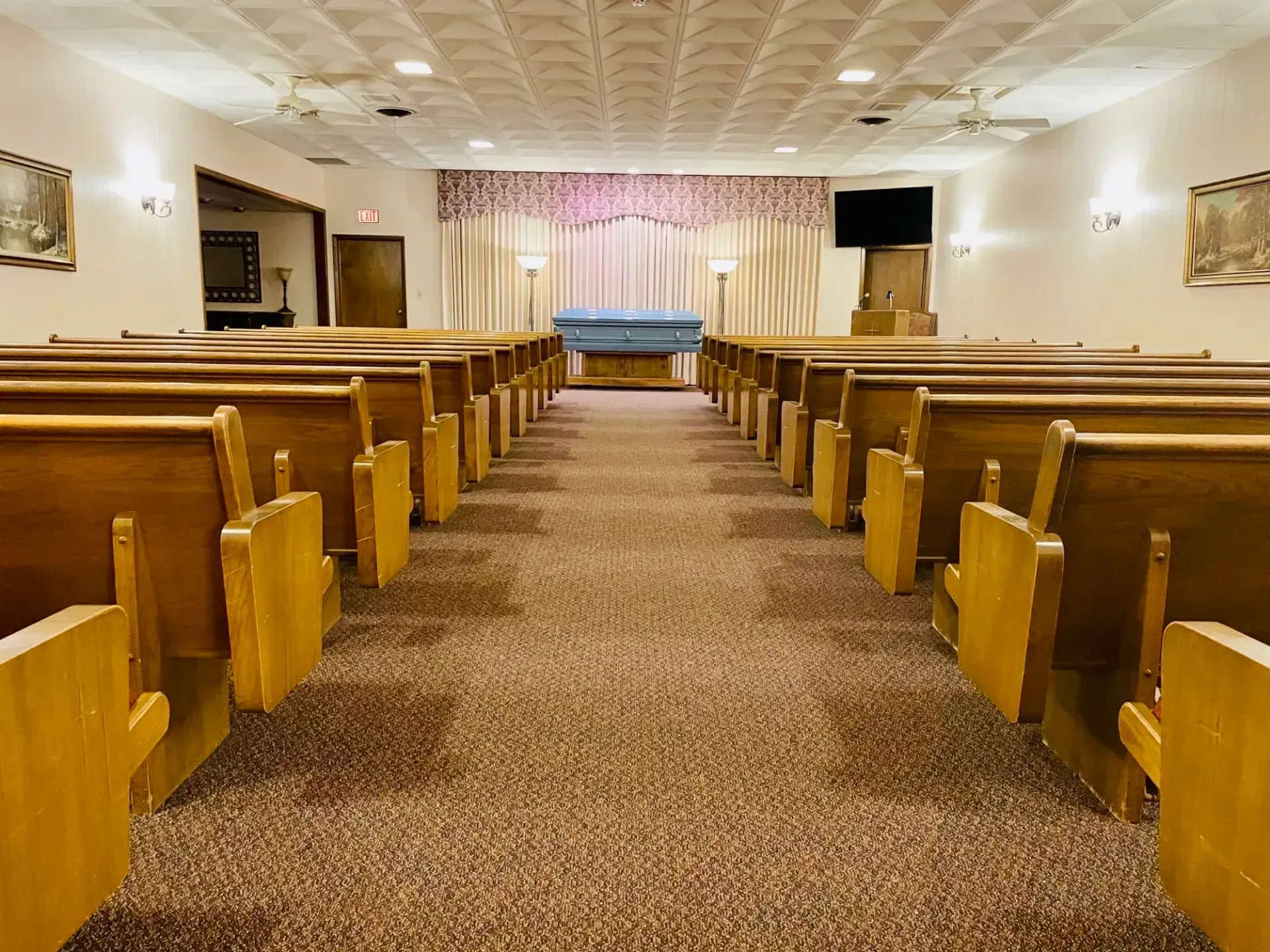 Empty chapel with wooden pews, carpeted aisle, and blue-draped altar at the front
