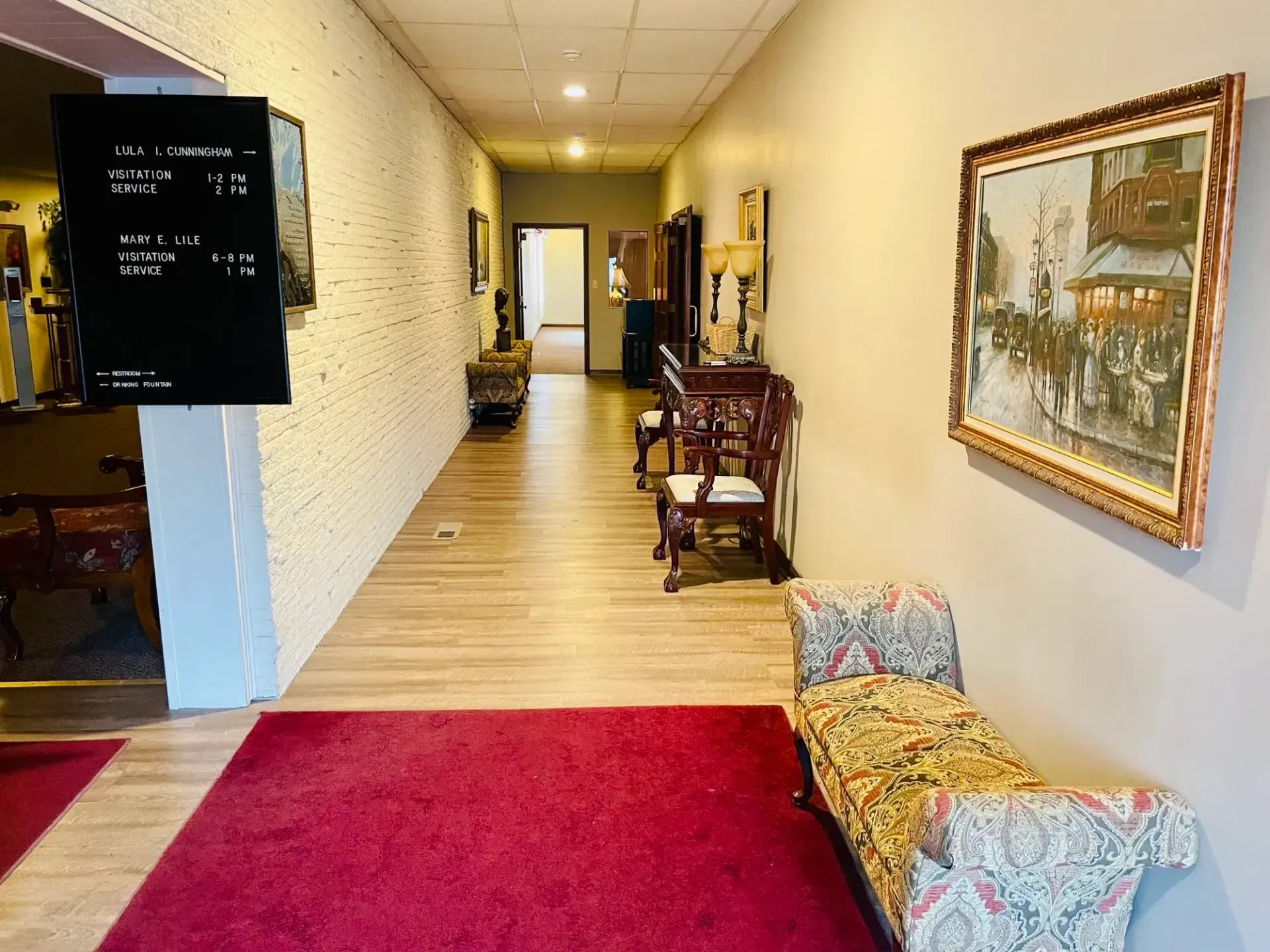 Long hallway with red rug, framed art, and patterned benches in a warm-lit interior