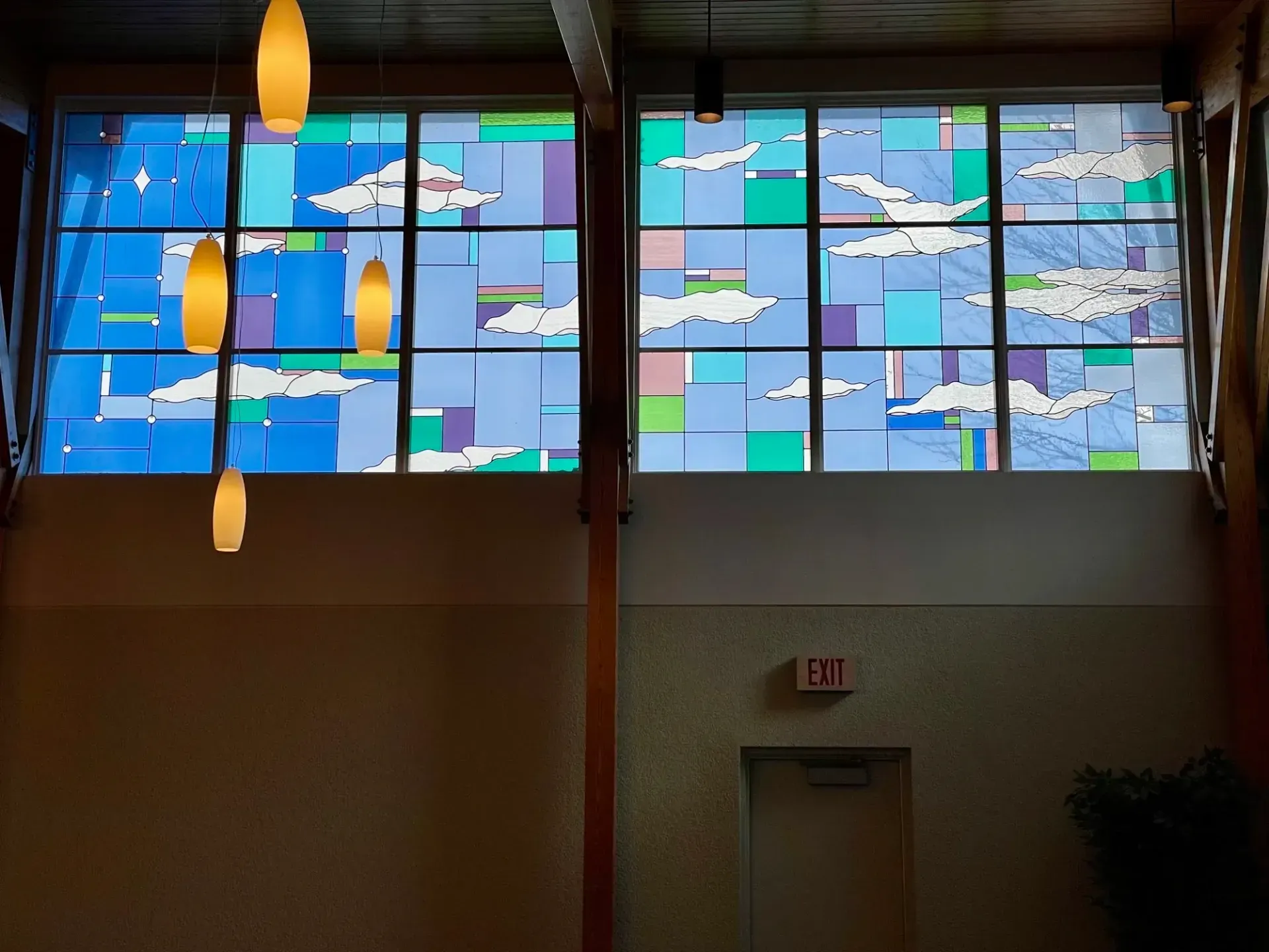 Stained-glass window above a doorway in a dim interior, showing blue sky and white clouds.